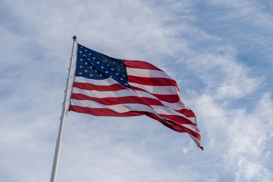 An American flag flying from a white flagpole against a blue sky with thin clouds