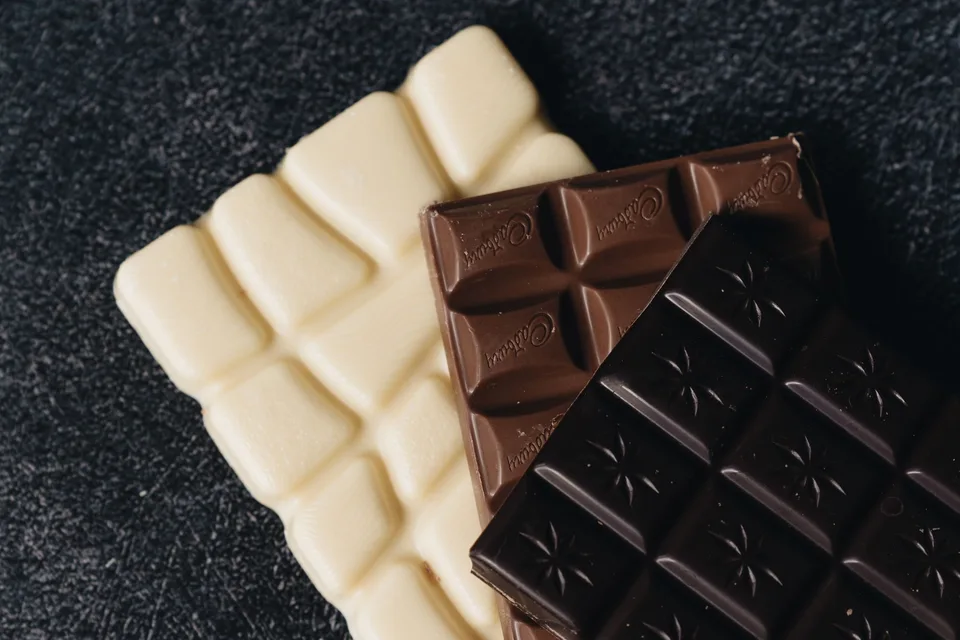 Three chocolate bars, white, milk and dark, fanned out on a dark countertop