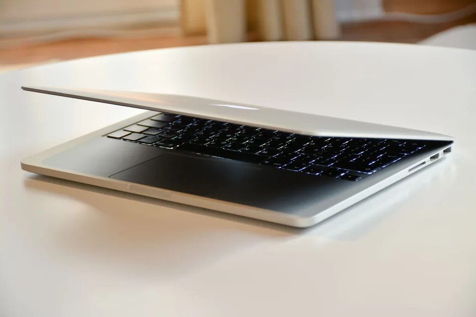 A silver laptop with its lid half closed on a white table