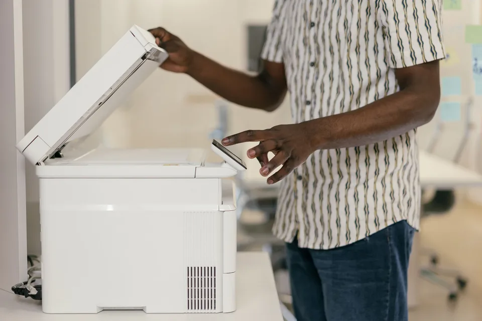 A man lifting the lid of a white desktop copier and pressing its control panel